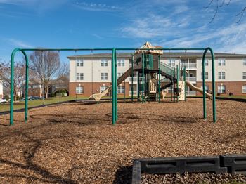 A playground with a slide and swings in front of a building.